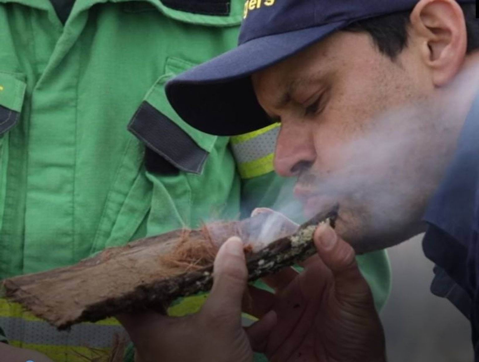 Indigenous Man blowing smoke from a broken off tree bark