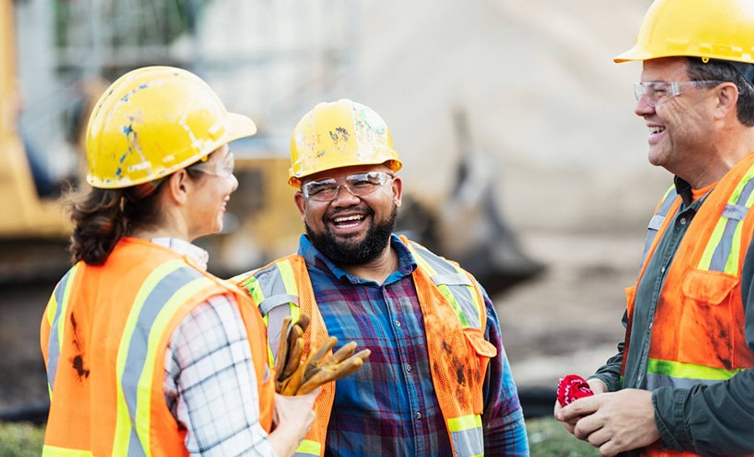 Three people standing and talking outside, while wearing high visibility safety vests.