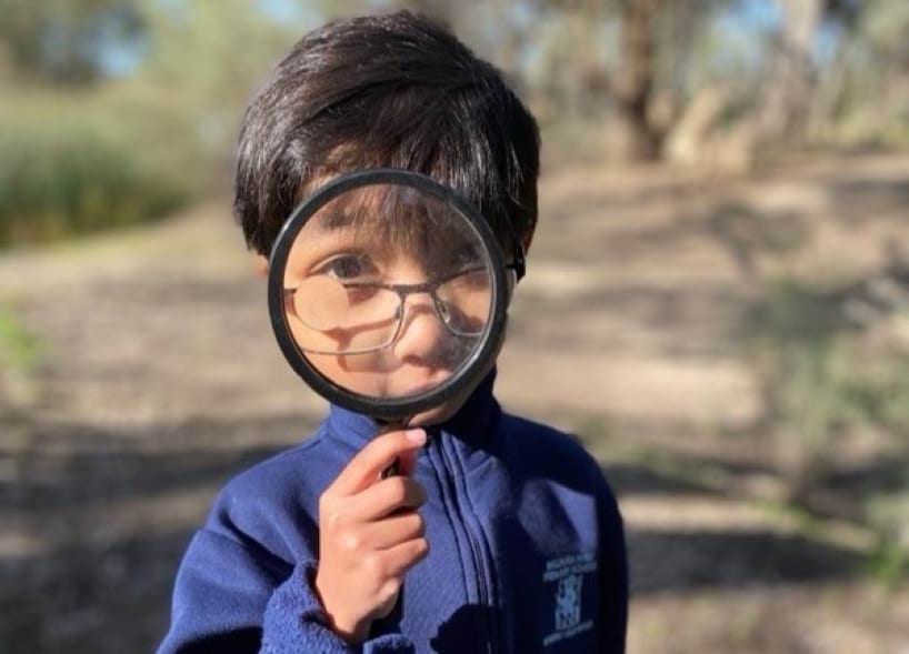 A child is holding a magnifying glass to their face and looking straight at the camera