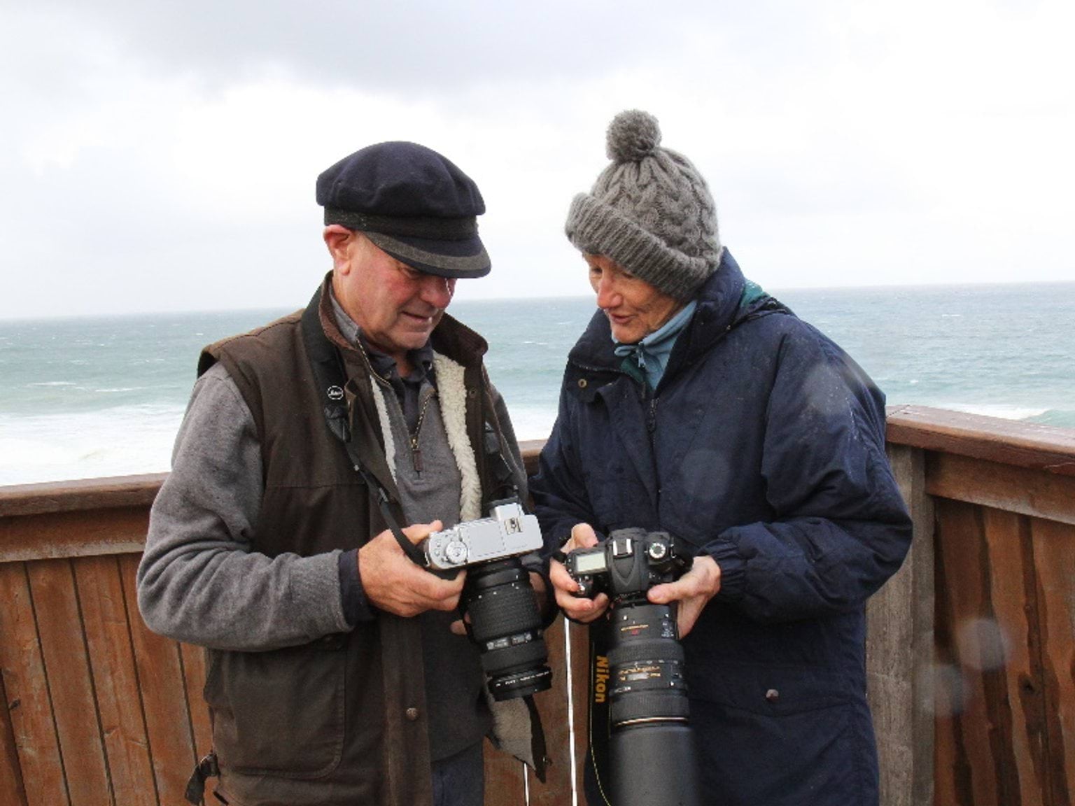 Two people holding cameras with both looking at the screen of one