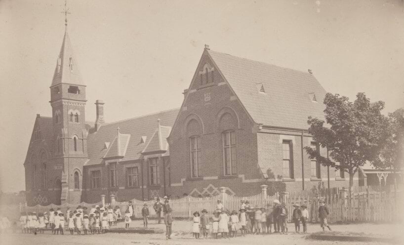 Black and white photograph of Colac Primary School building with students in front of the school gate. 