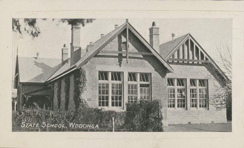 Black and white photograph of the Wodonga school building. The building is brick and has ivy growing up the side. The front fence has a hedge. 