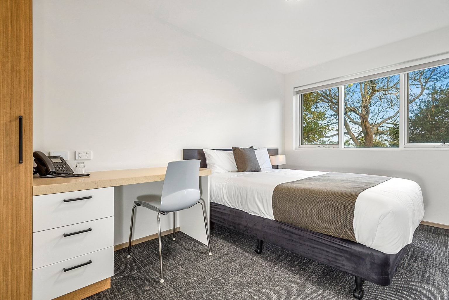 Image shows the VEMI accommodation. A bed, desk, chair, wardrobe and chair in a room