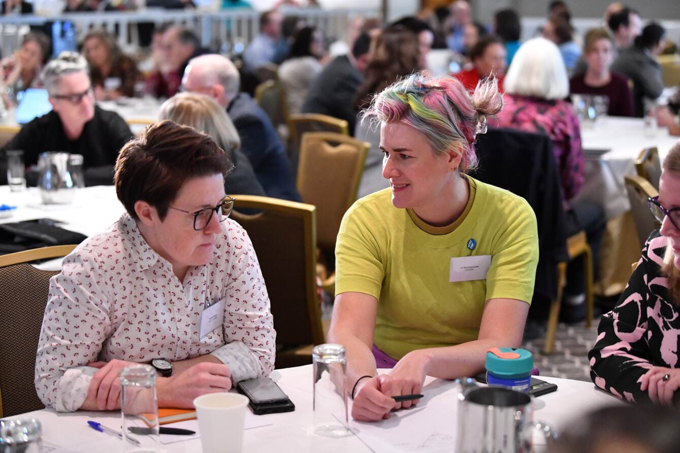 Two attendees of the Collaborative Centre Forum engaging in conversation during a table activity