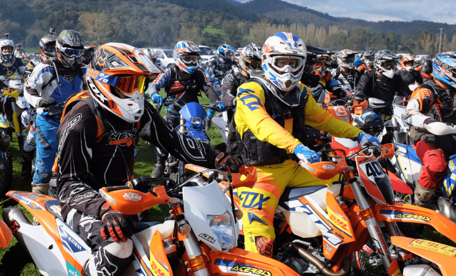 A large group of trail bike riders sitting on their motorcycles and wearing colourful helmets and other safety clothing