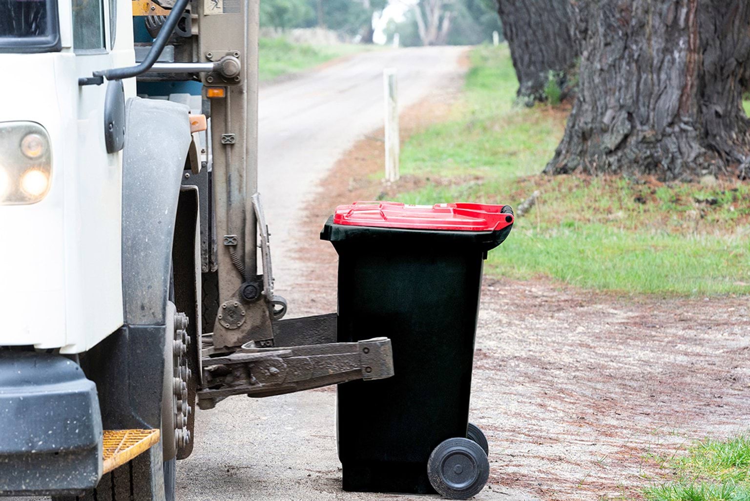 Roadside collection of red lidded wheelie bin by council truck