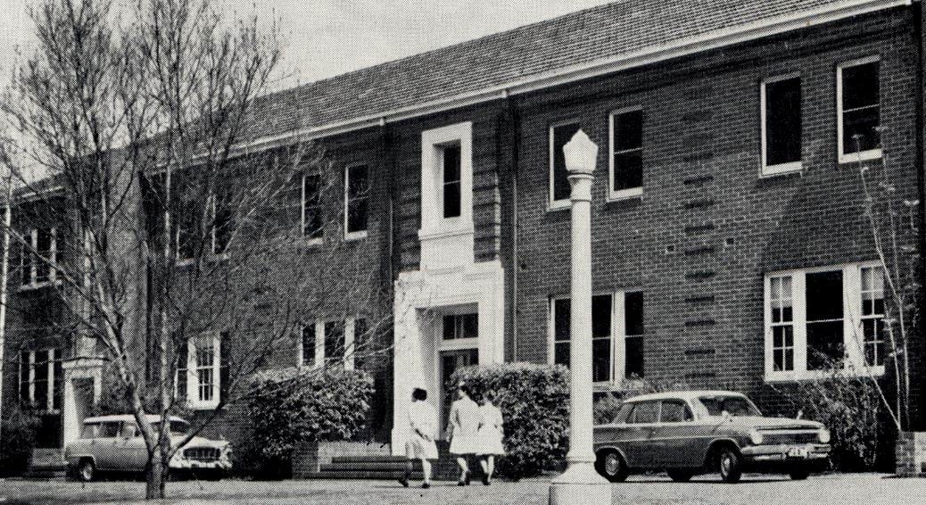 Front of brick building with large windows and three women walking in front.