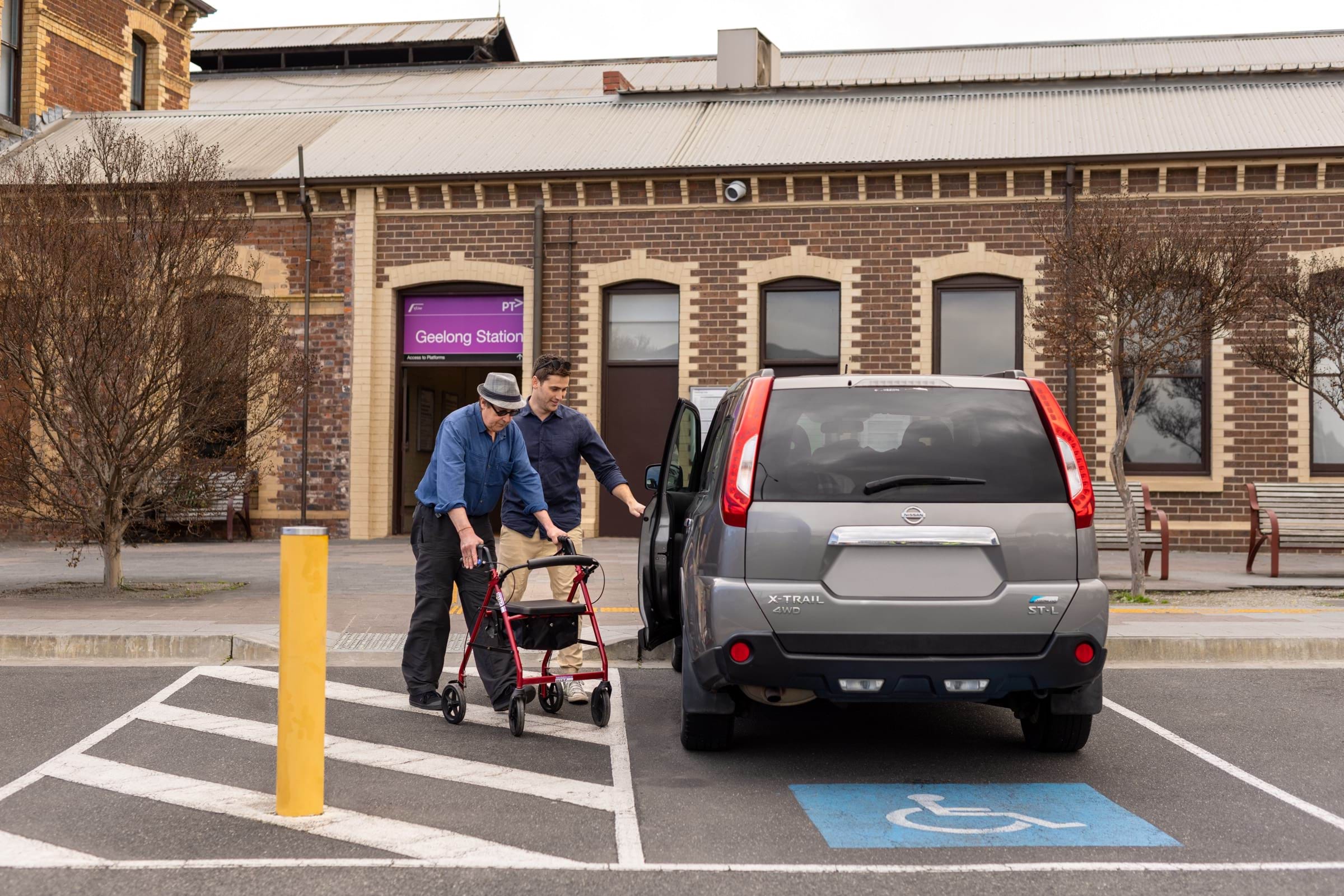 Image of person using a walker about to enter a car in an accessible parking spot outside Geelong Station.