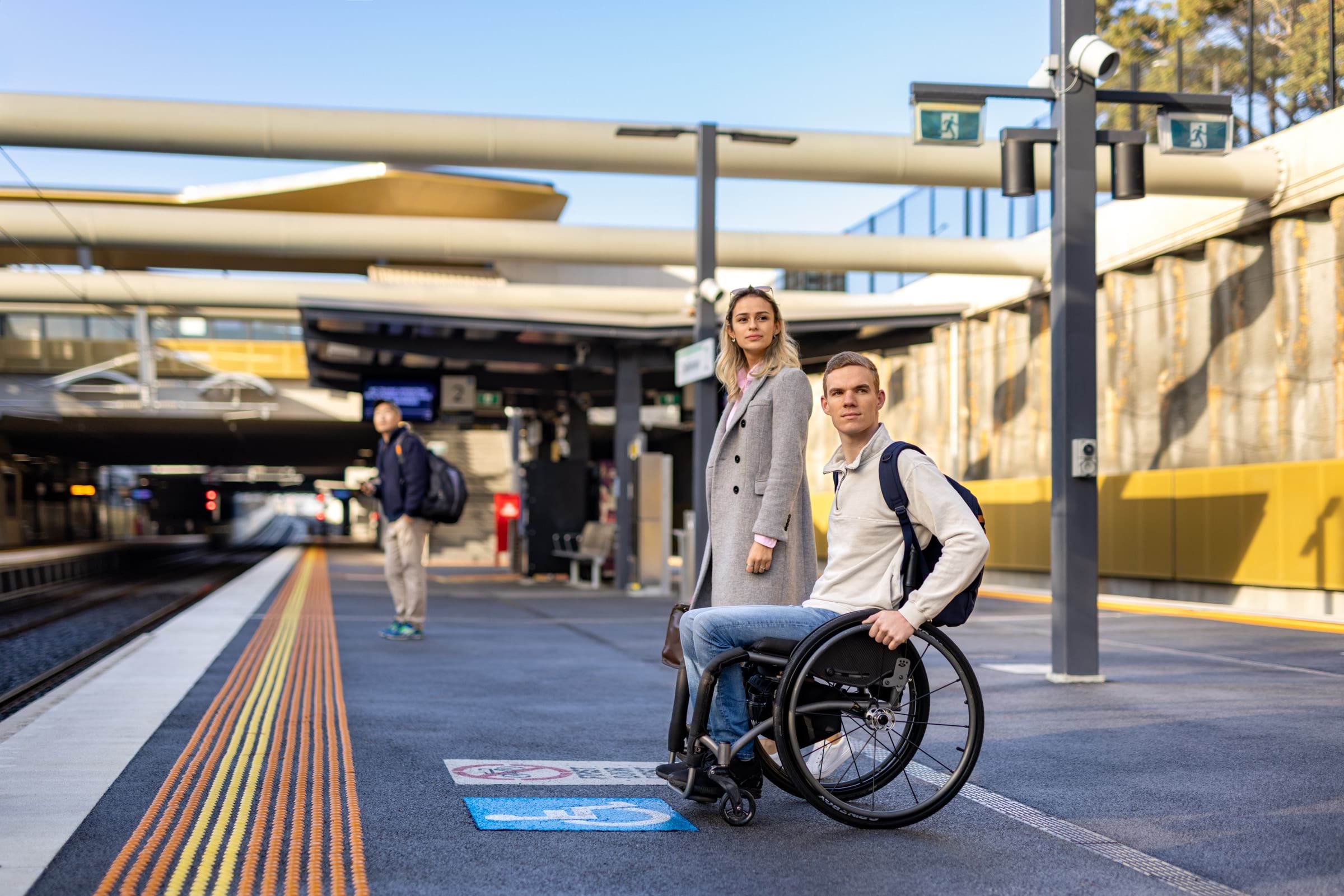 Image of two people, including one wheelchair user, waiting at the first door boarding point on a train platform.