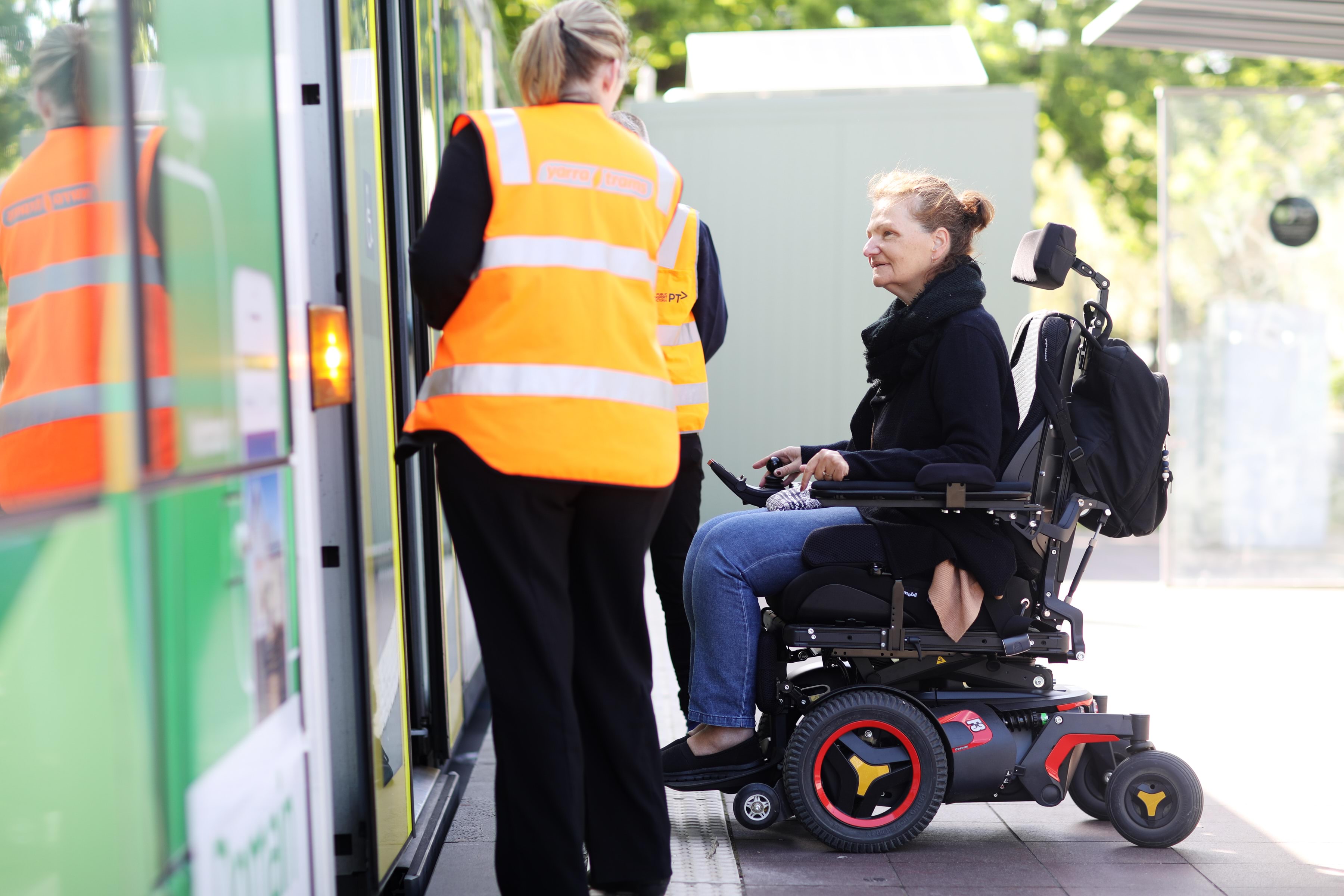 Person travelling with mobility device interacting with staff as they board a tram.