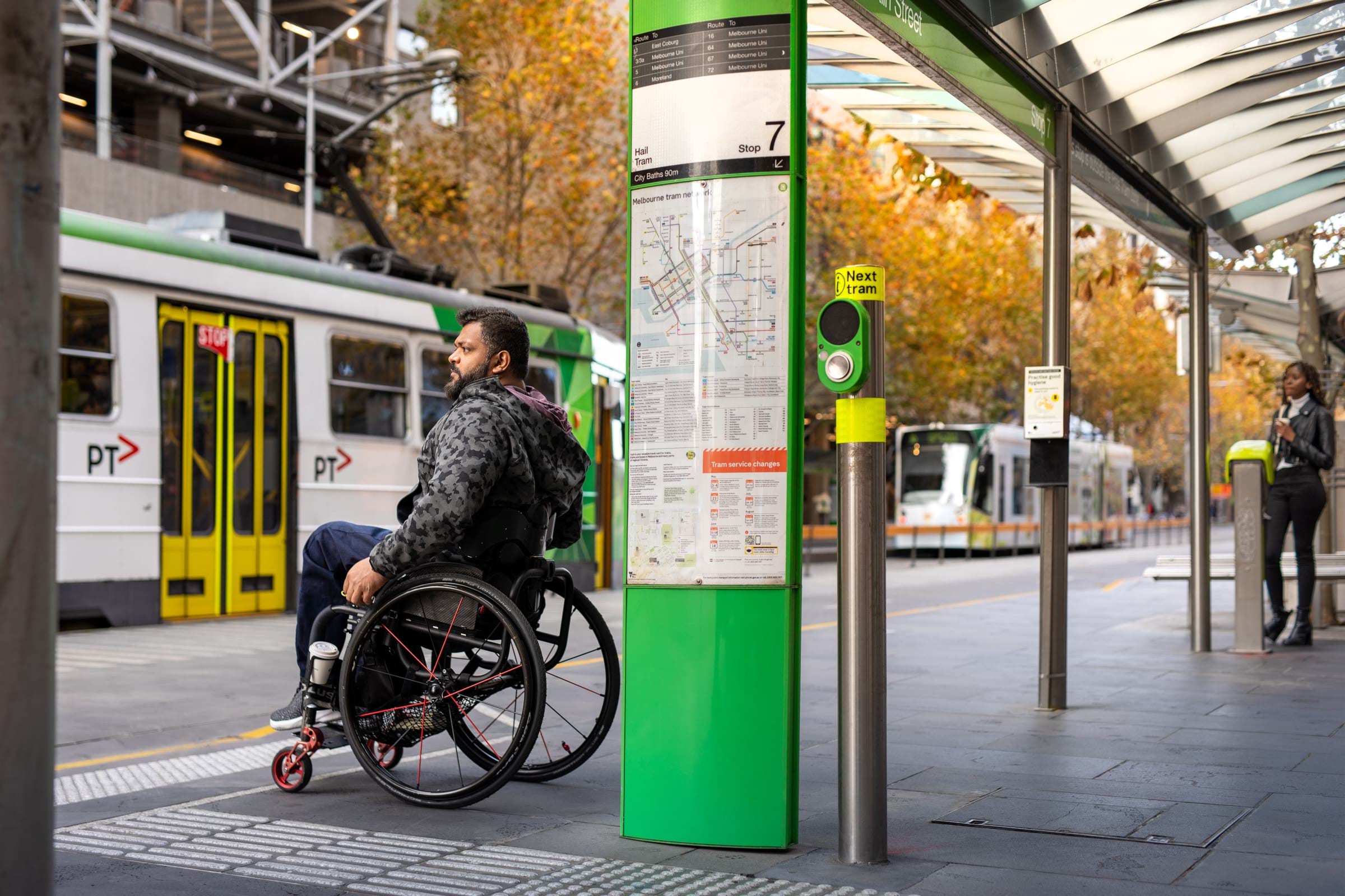 A person using a wheelchair waiting at a level access tram stop.