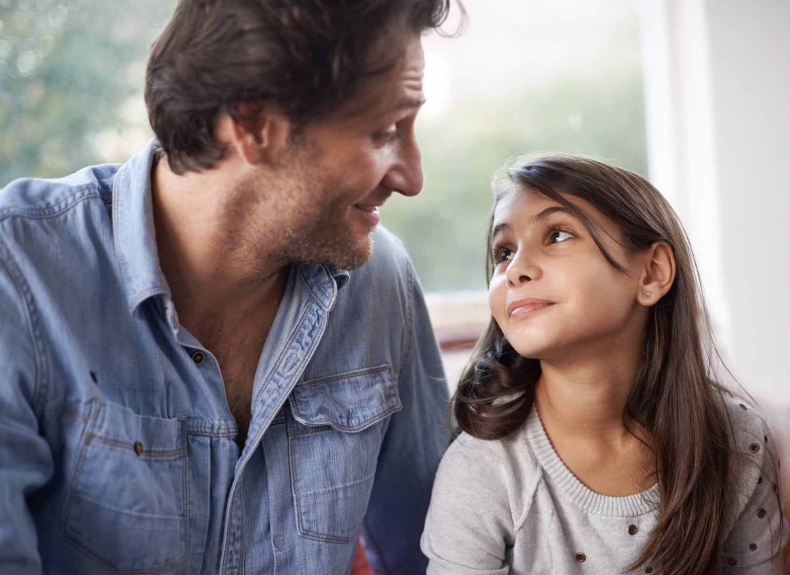 A man and teenage girl sitting in front of a window looking at each other.