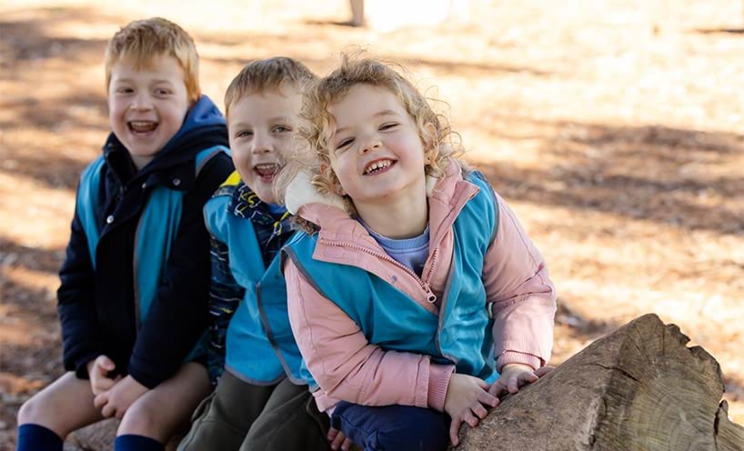 Three smiling children sitting on a log