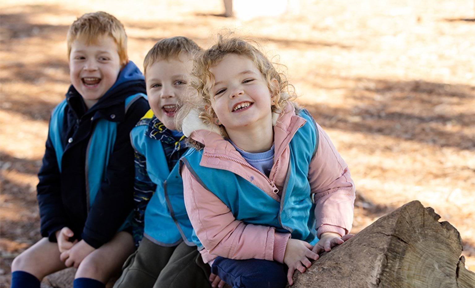 Three smiling children sitting on a log