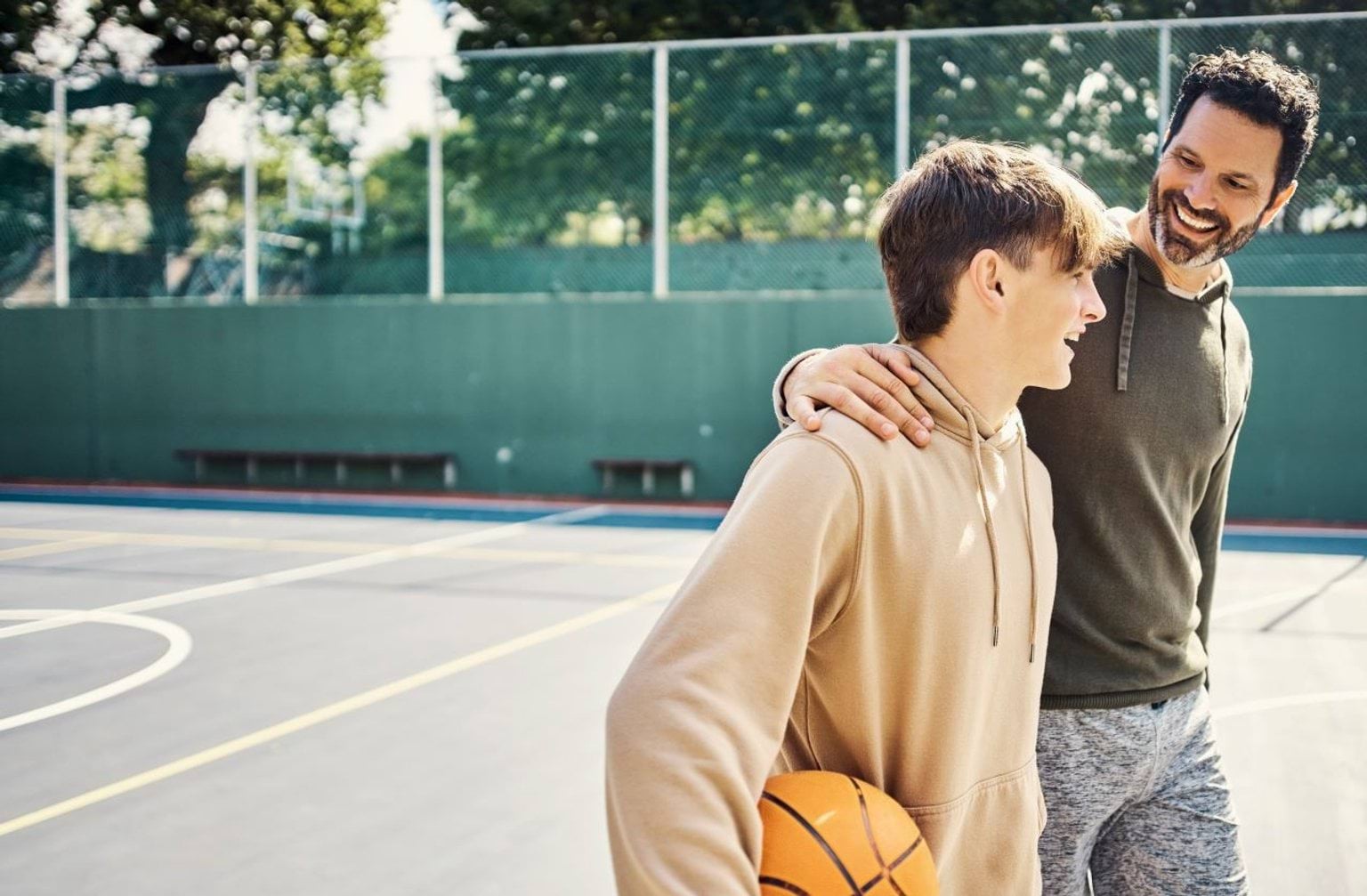 A man and teenage boy walking across a basketball court.