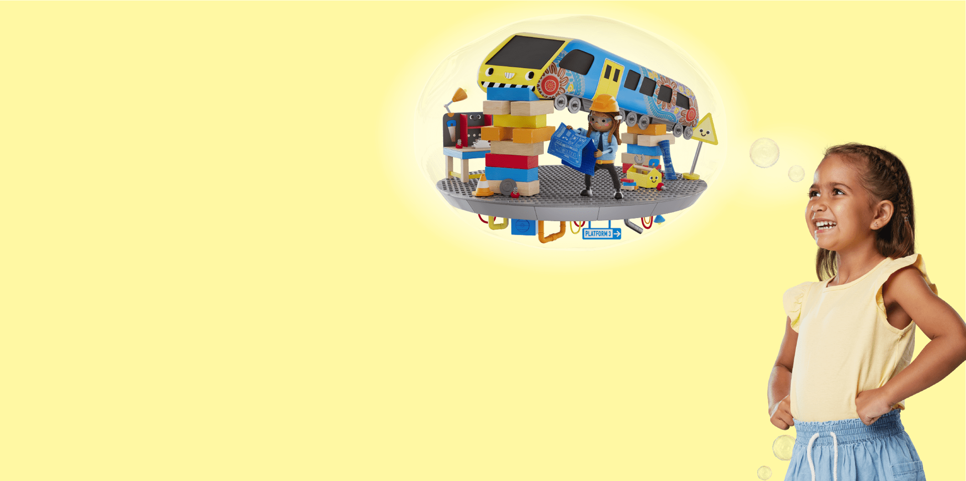 A young girl smiles and looks toward a thought bubble showing a colourful construction scene. Inside the bubble, a cartoon builder in a hard hat holds blueprints while standing on a train platform, surrounded by stacked blocks, tools, signs, and a cheerful train decorated with bright patterns. The background is soft yellow.