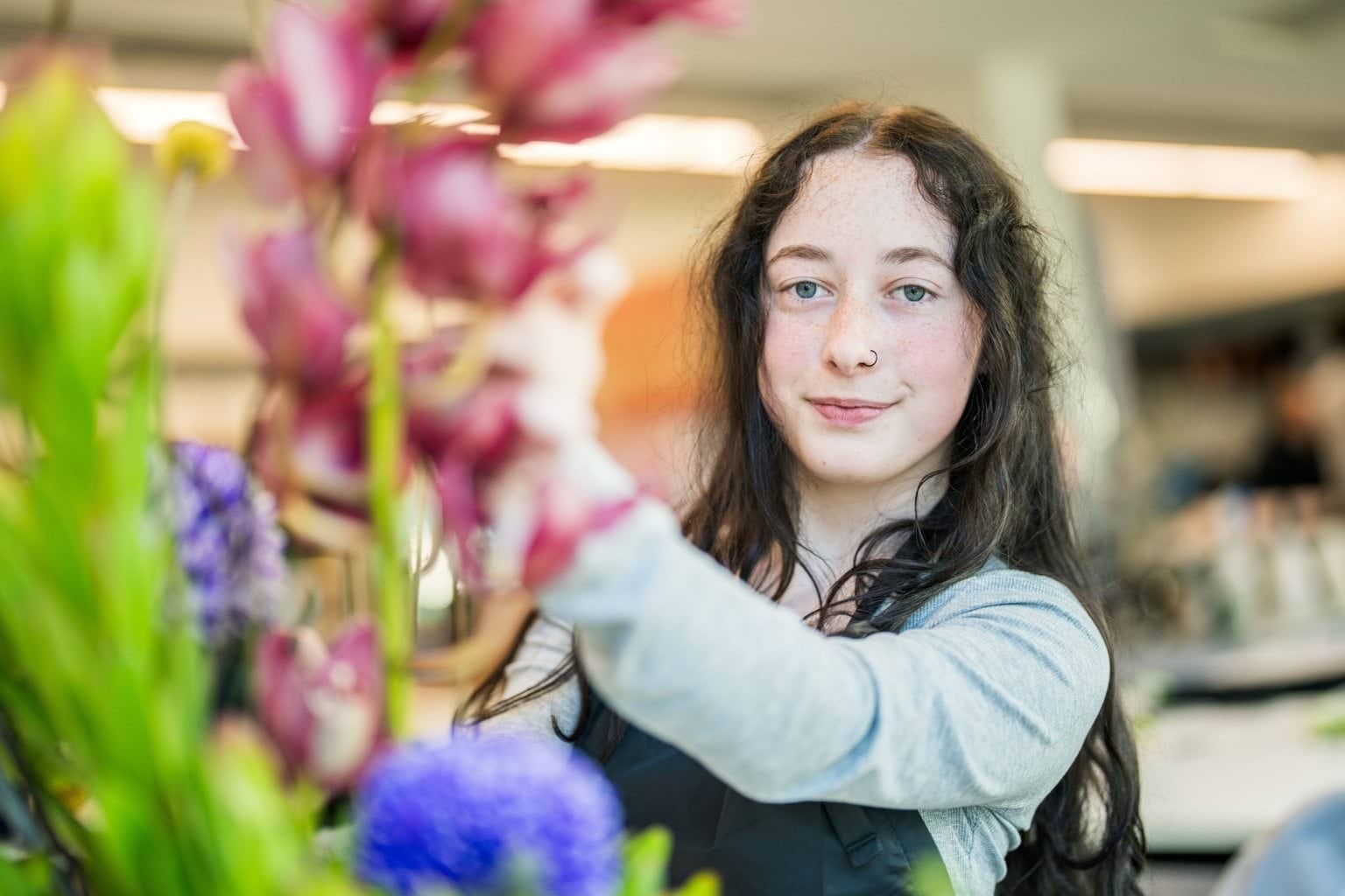 A person with dark hair arranges a brightly coloured floral arrangement.