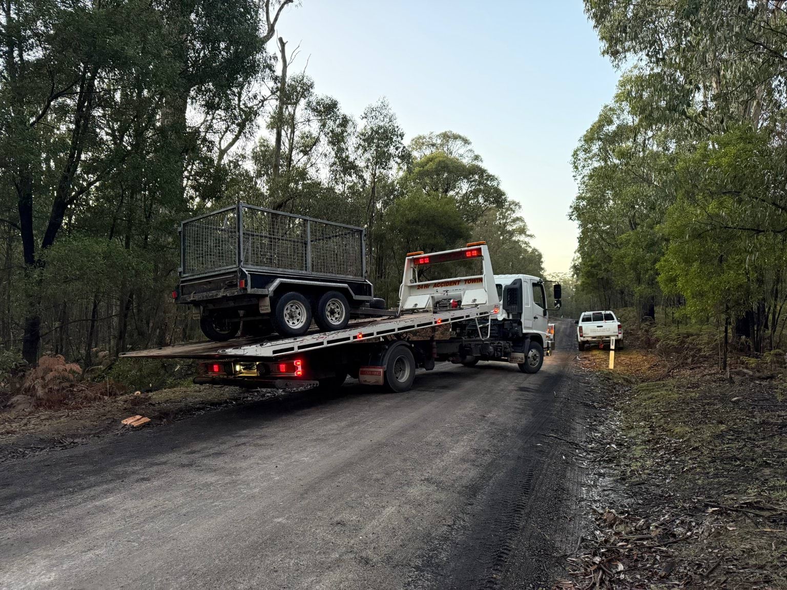 A trailer on the back of a tow truck on a road through the forest