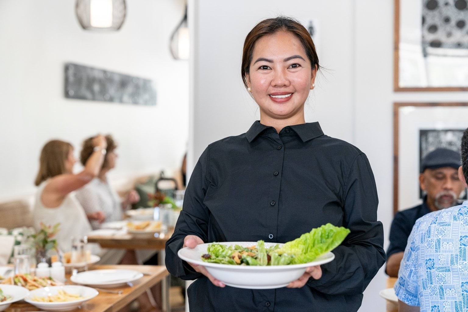 A smiling person carries a bowl of salad in a cafe.