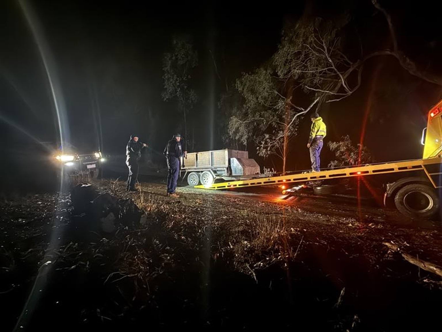 Three people loading a confiscated trailer onto a tow truck at night