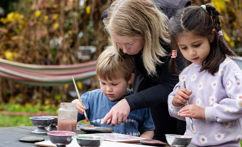 An educator assisting two children paint