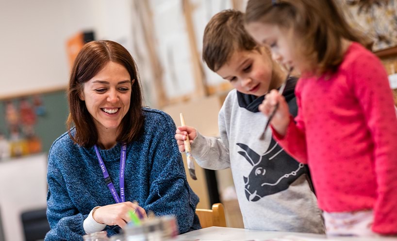 An educator assisting two children paint