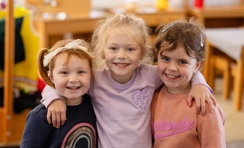 Three children smiling with arms around each other's shoulders