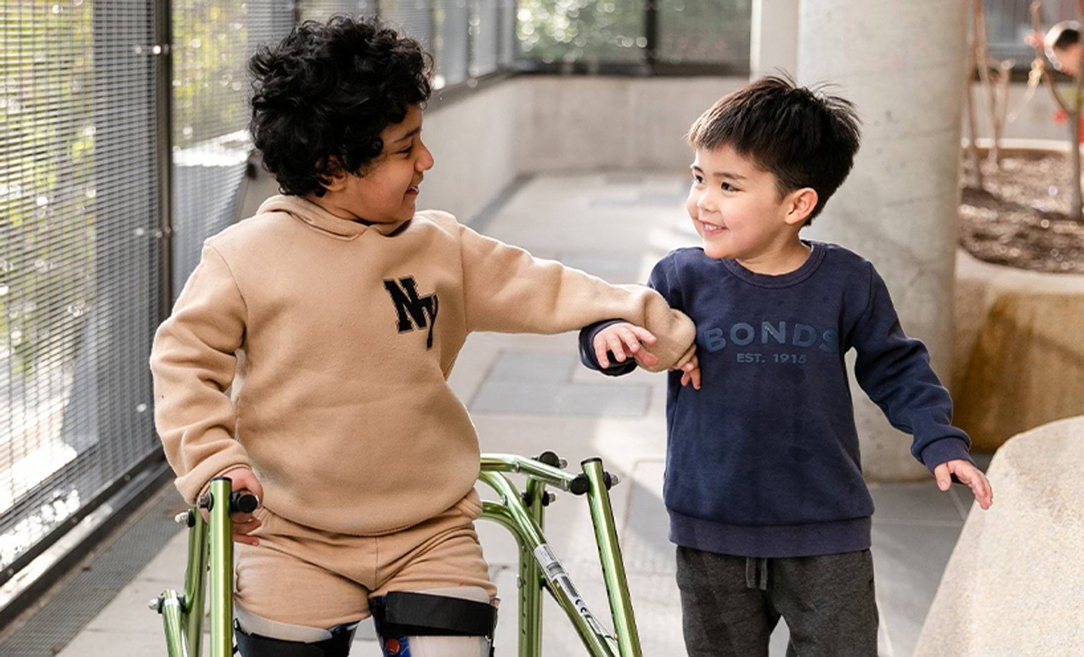 A child in a walking frame holding hands with another child