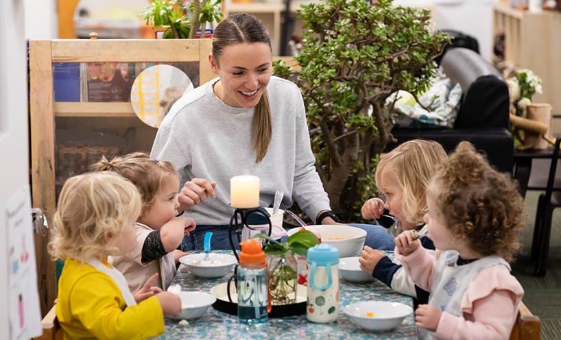 An educator sitting with children at their table while they are having their food