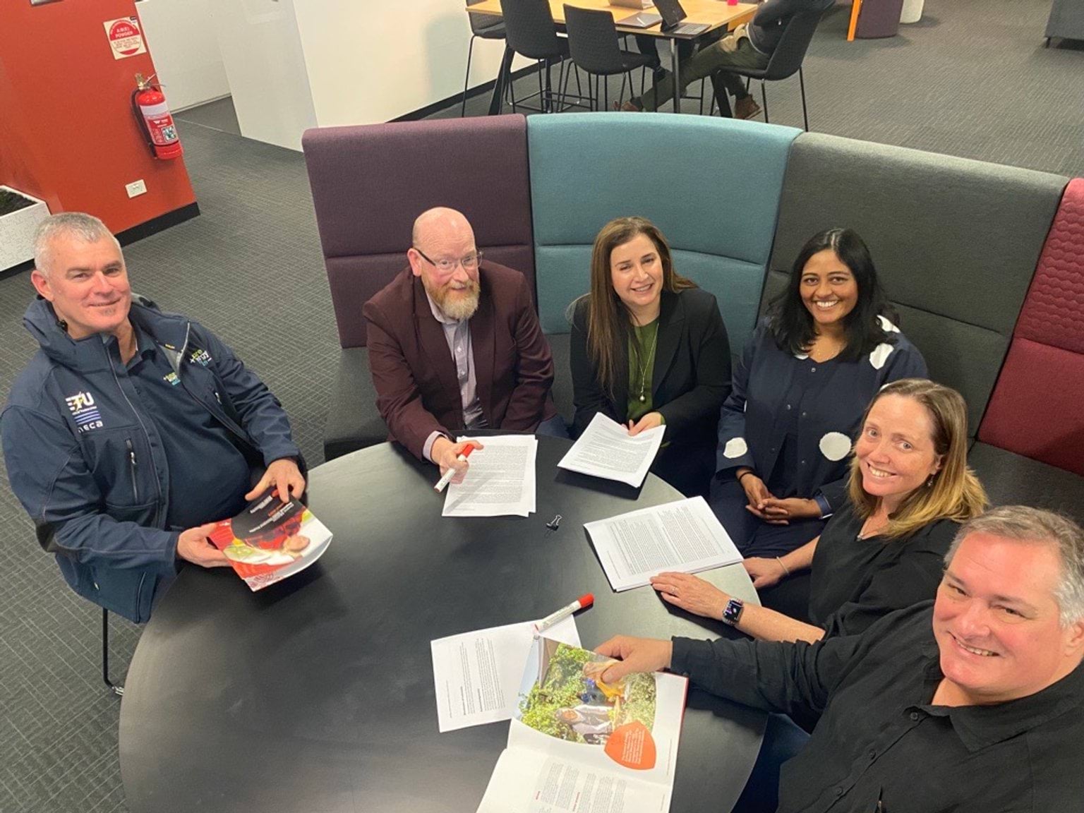 Six people sitting around a table smiling into camera 