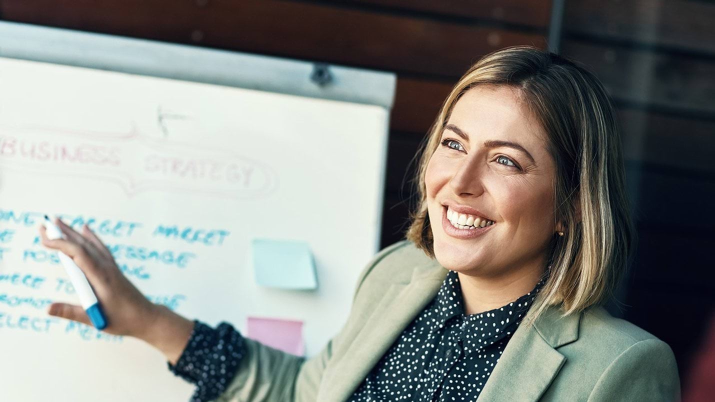 Woman smiling while pointing at a whiteboard 