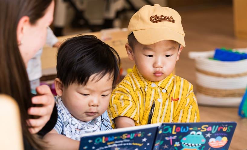 Teacher and 2 small children reading a book.