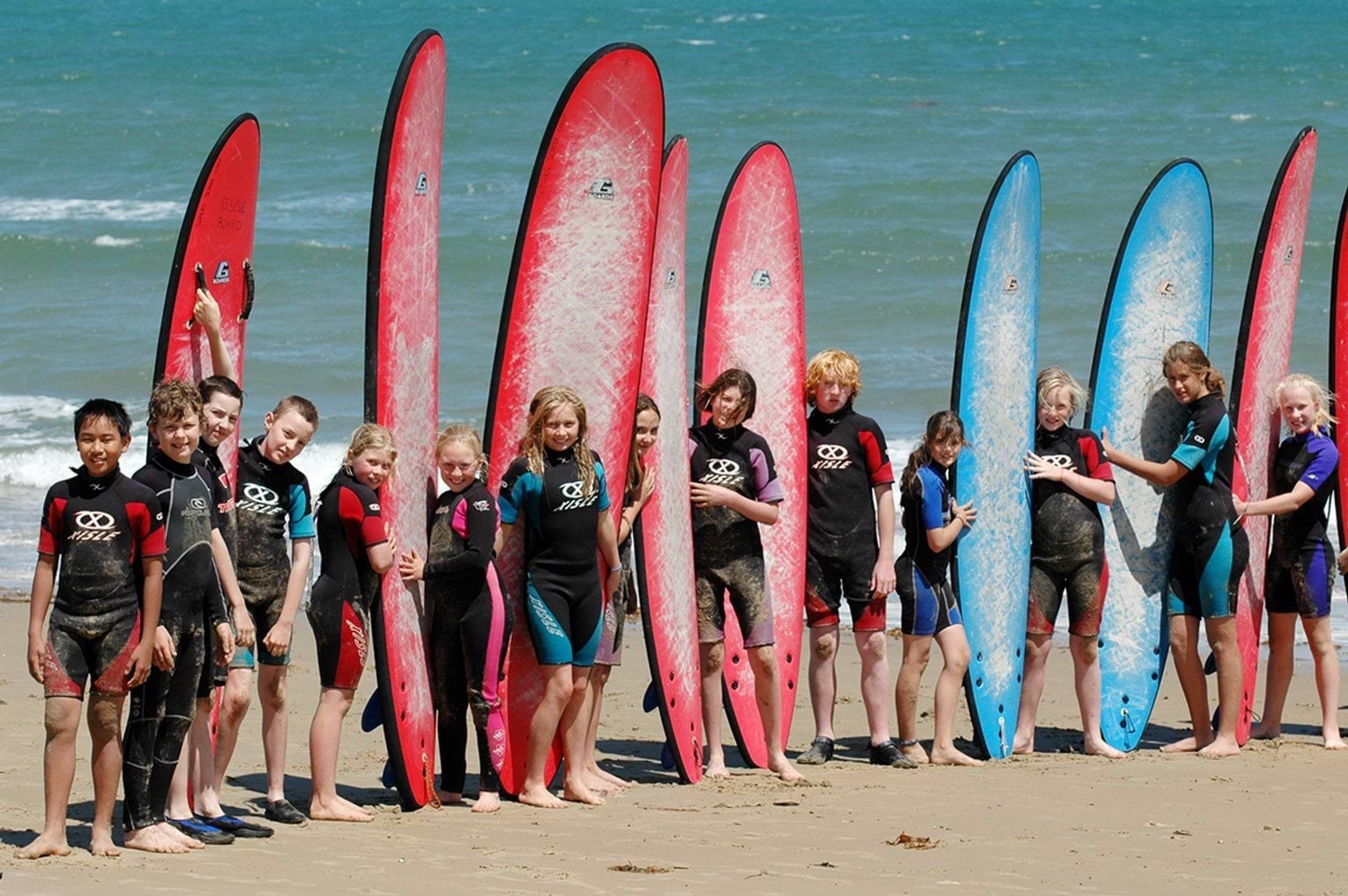 A group of kids stand next to long and short surfboards