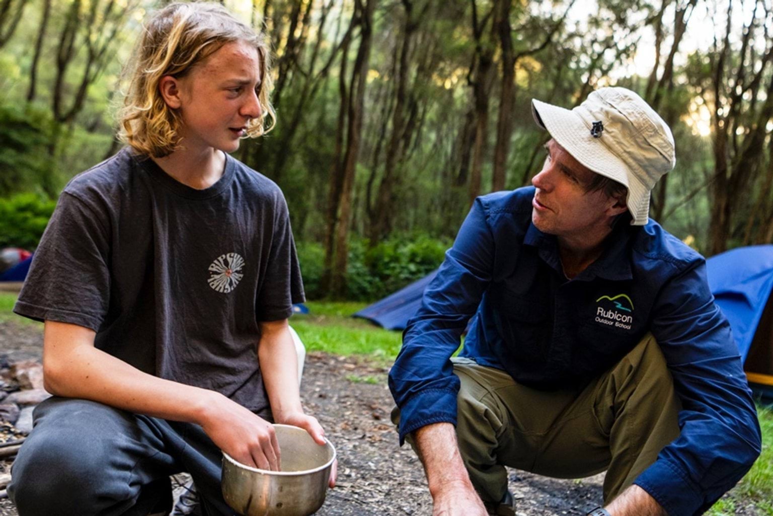 Student and teacher in bushland interacting as they kneel