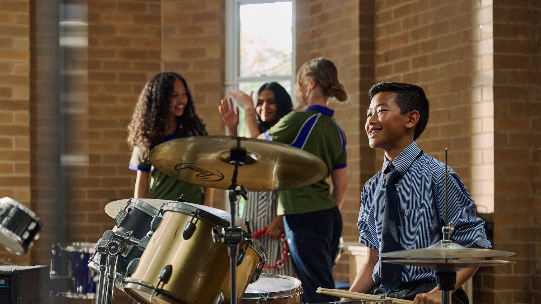 A group of school students in a music class with a student in focus playing drums