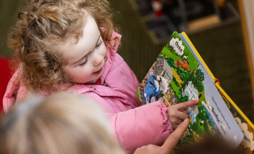 A child being read a picture book while they point at the picture