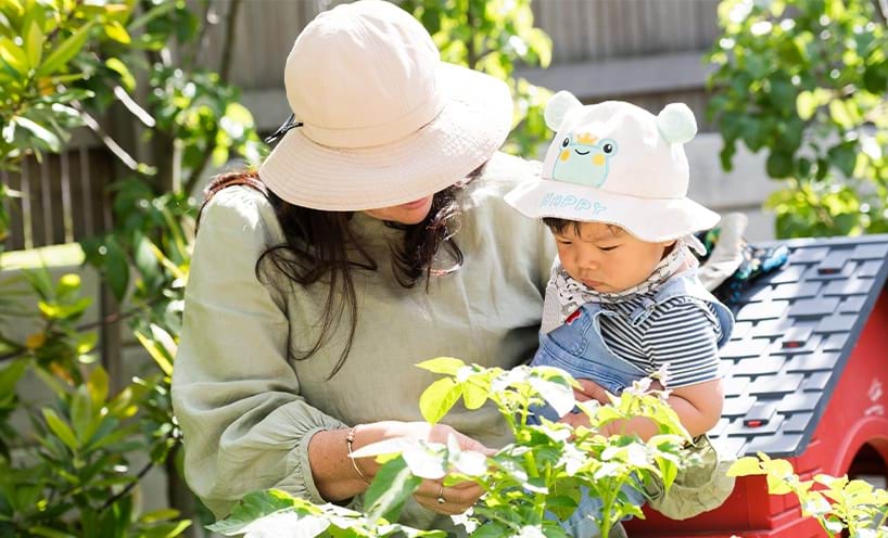 Teacher showing a small child a green plant and the child is looking closely at the leaves.