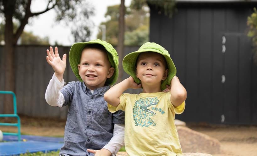 Two toddlers sat outdoors with their sun hats on
