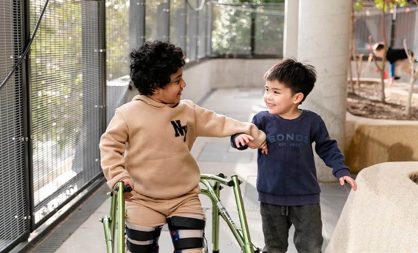A child with walking frame being helped by another child