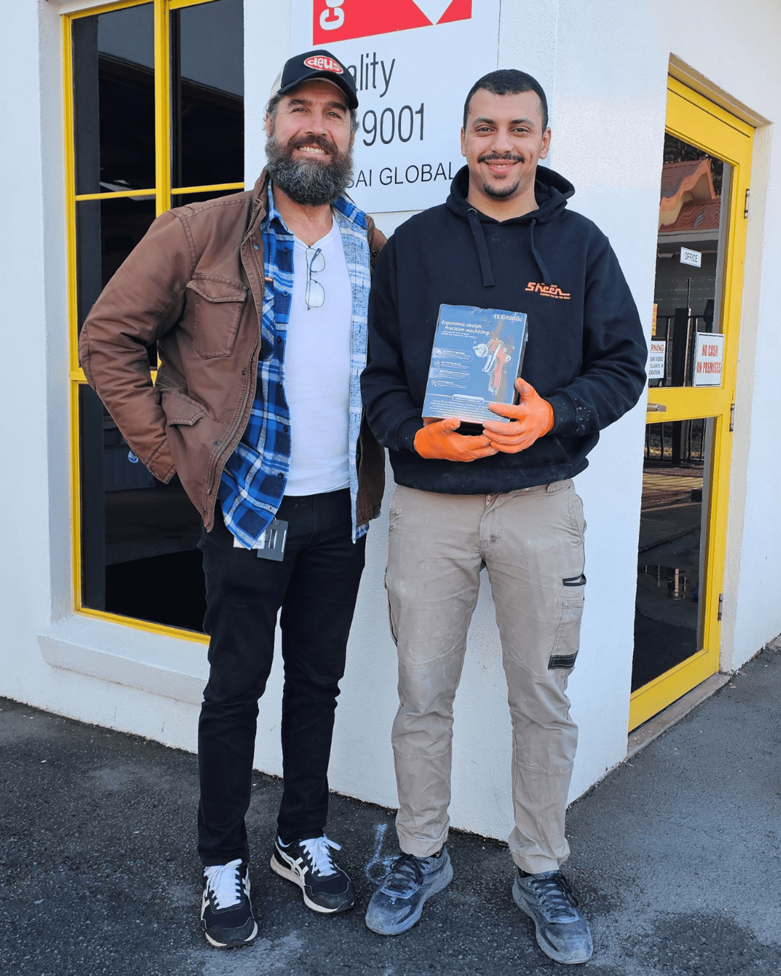 Sahin is standing outside smiling next to Anas who is holding a spray gun box.