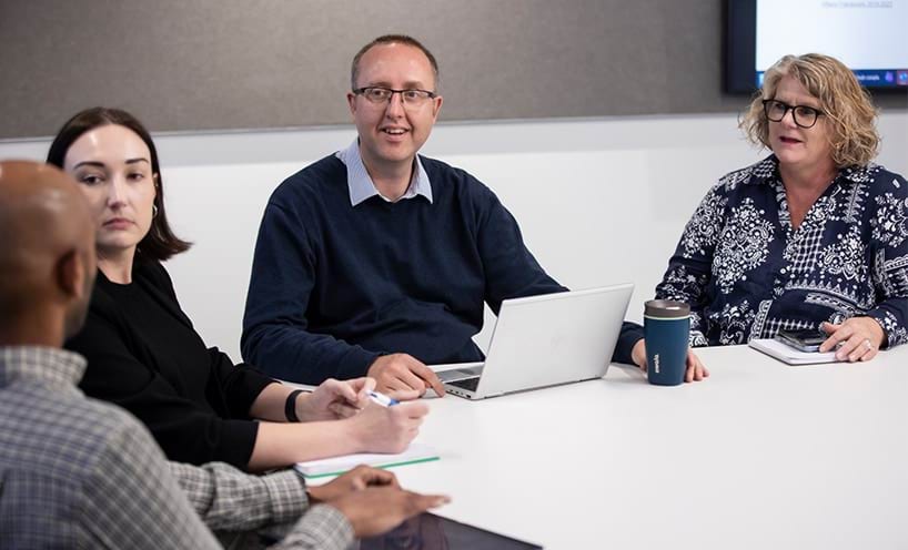 Staff sitting around a table with laptop and notepads at an information session.