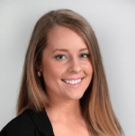 A photo of Claire Sanders. She is looking at the camera and smiling, with long brown hair and a black top.