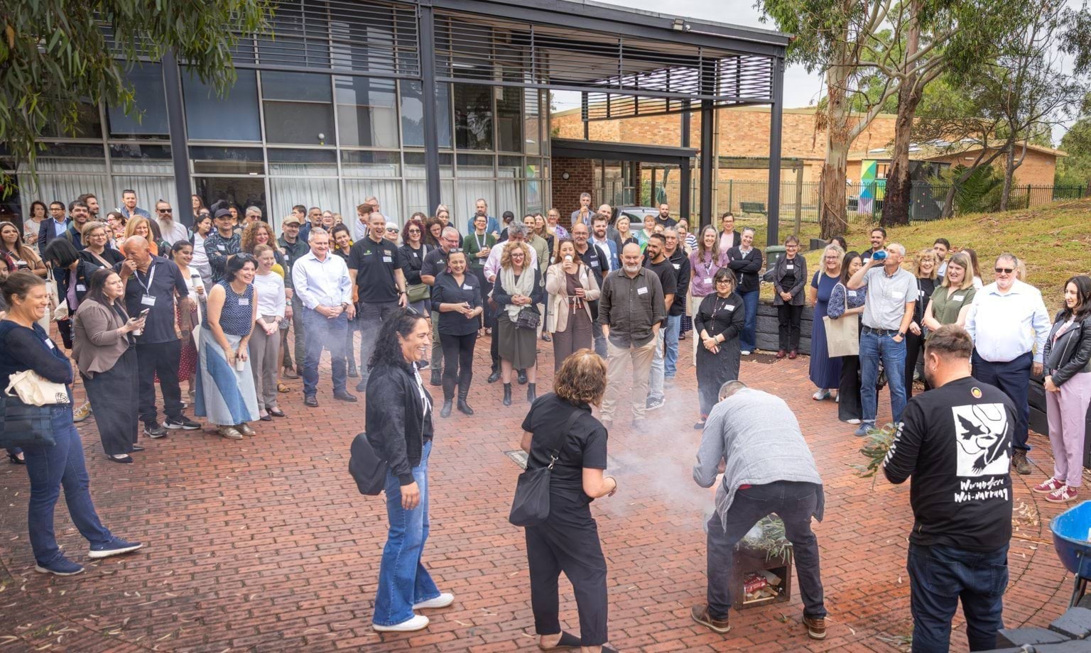 People standing around in a group watching an Aboriginal smoking ceremony 