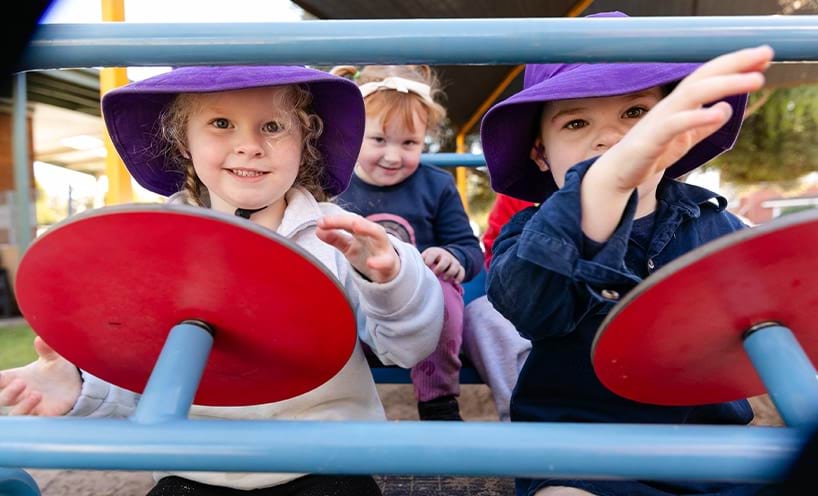 3 children sitting on a toy car with the two of them sat on the front seats with steering wheels