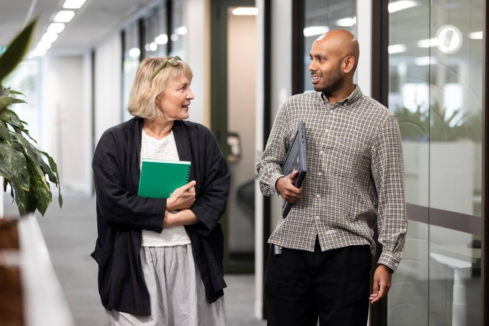 Two people walking down a hallway in an office.