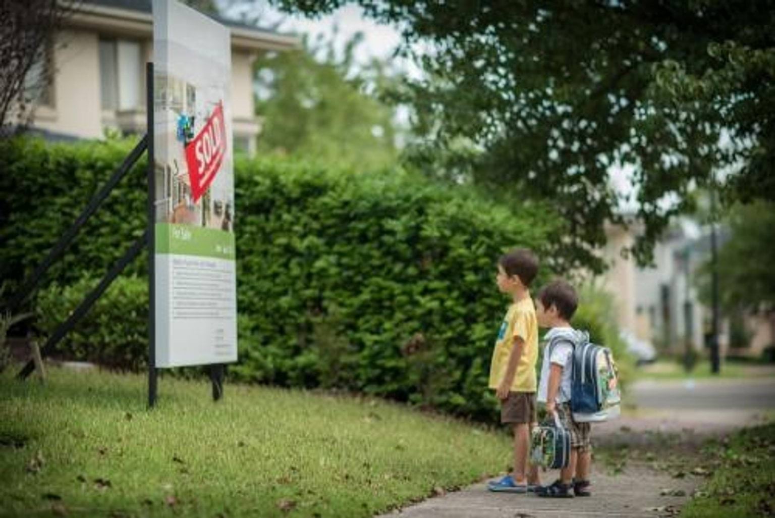 Two children in front of house sale sign