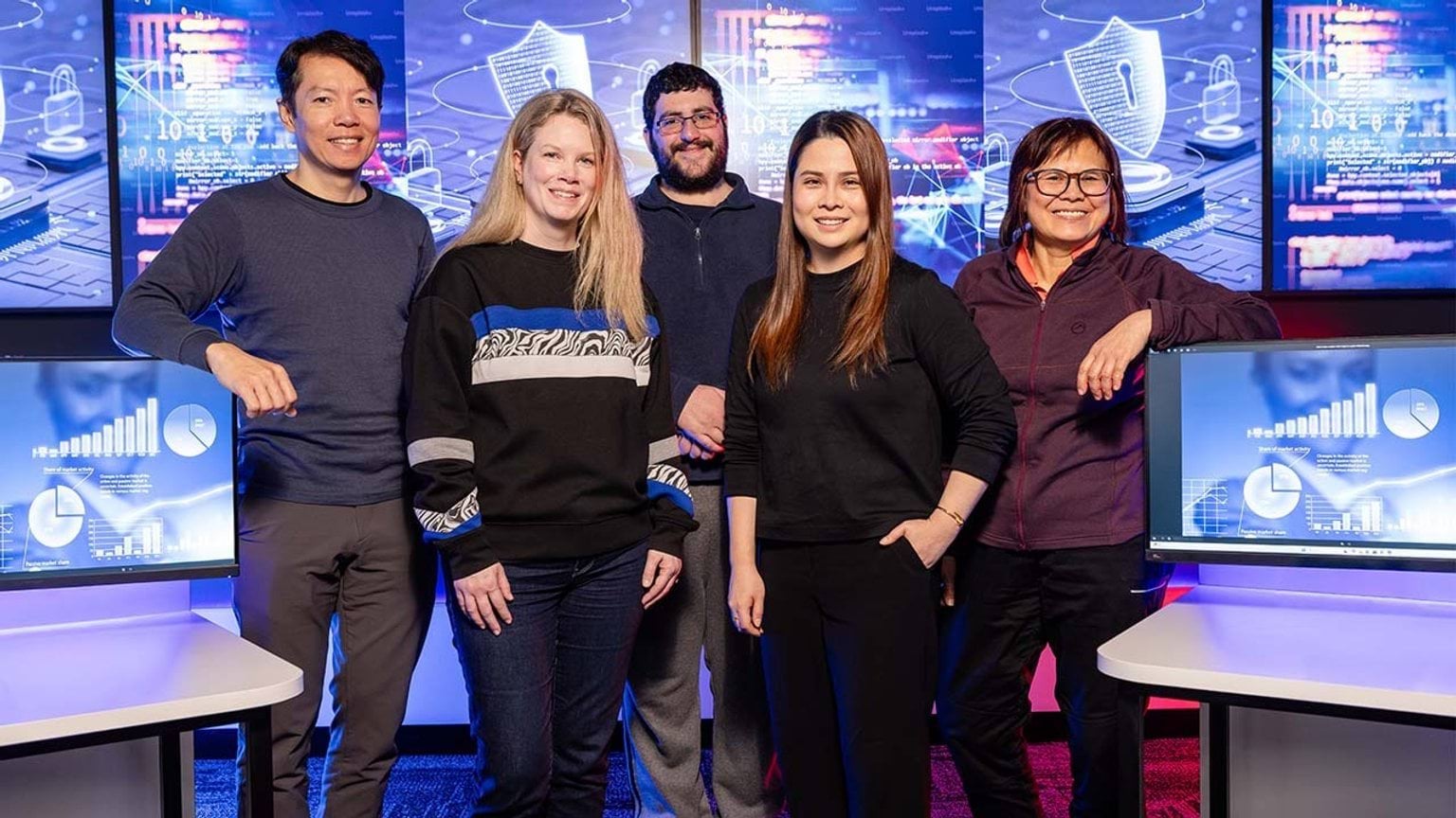 A group of 5 students and trainers standing in a computer lab looking at the camera