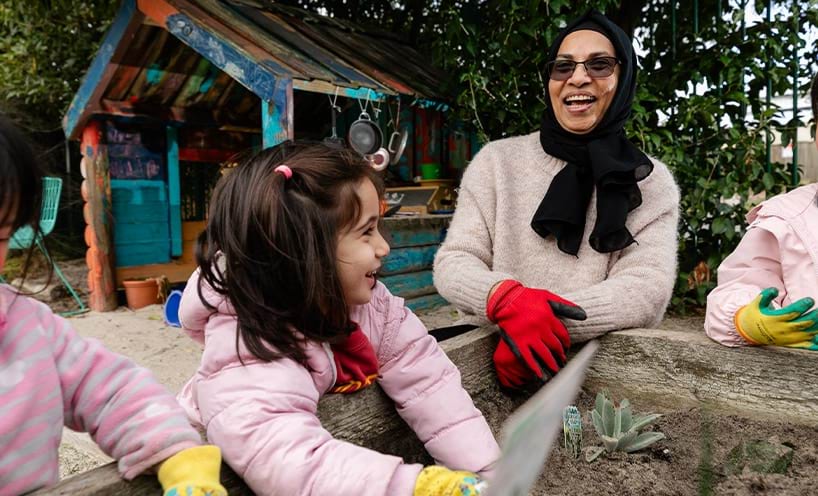 An educator assisting children garden