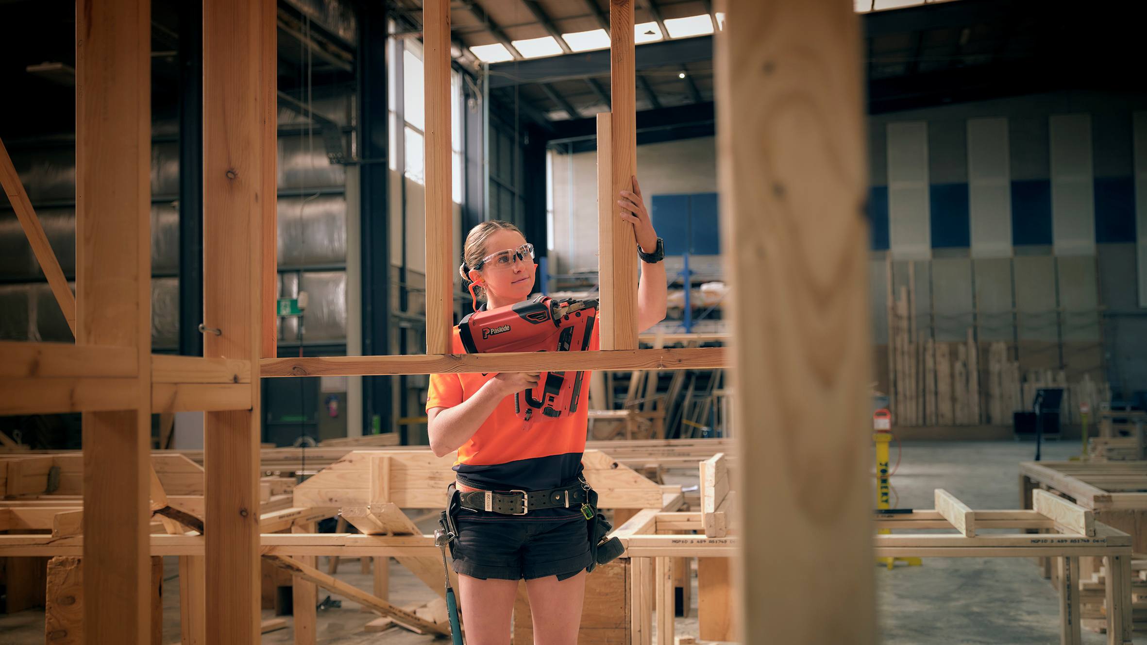 Clea using an cordless nailer to build a frame on a construction site