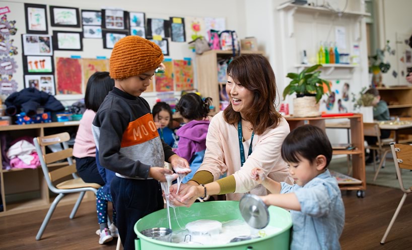 An educator with two children engaged in a sensory play with bubbles and dishes in a bucket